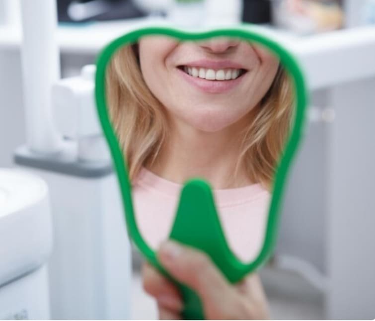 mujer sonriendo se mira en espejo dental verificando sonrisa